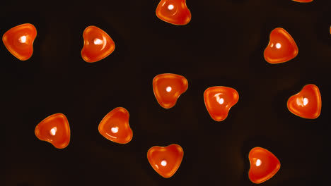 Overhead-Shot-Of-Romantic-Lit-Heart-Shaped-Red-Candles-Revolving-On-Black-Background-Being-Blown-Out